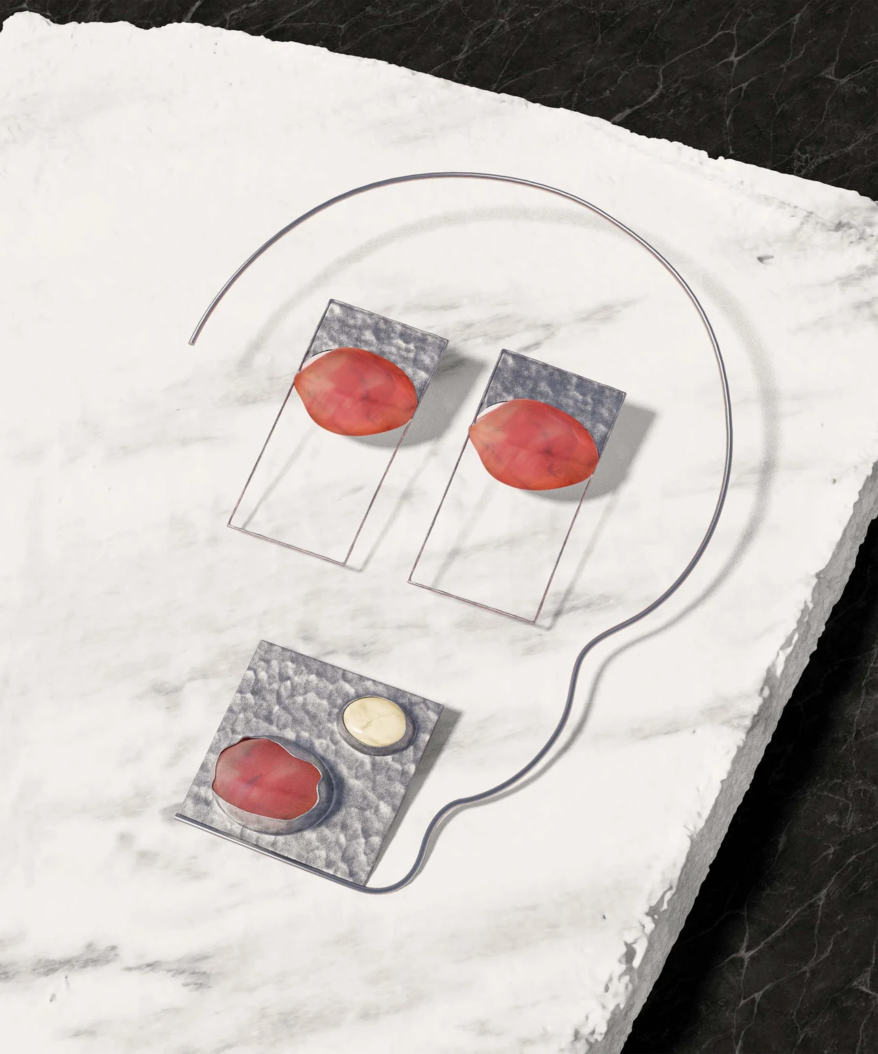 Silver earrings and a necklace with red stones and a pale detail are arranged on a white slab with an irregular edge.