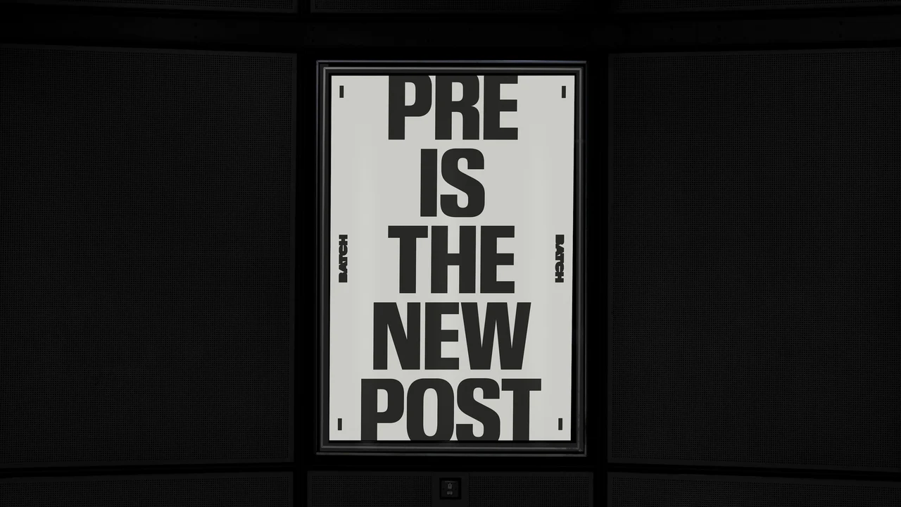 Illuminated vertical poster in a dark setting features “Pre is the new post” in very tall black letters on a pale ground with small side markers.