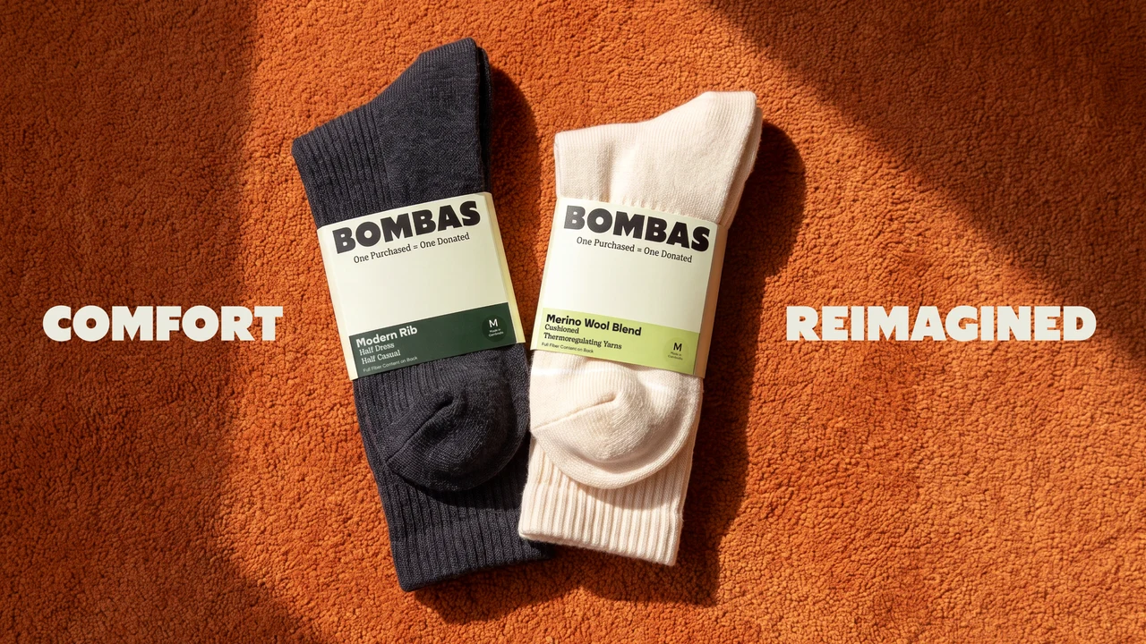 A navy and a cream pair of socks with BOMBAS paper bands lie on sunlit orange carpet between the words Comfort and Reimagined.