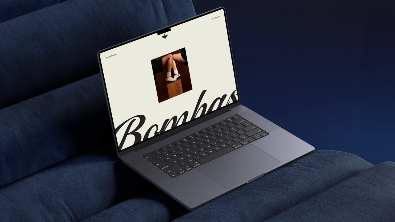 Laptop on a navy velvet sofa showing an off-white Bombas page with the script logo and a photo of crossed legs in white socks and heels.