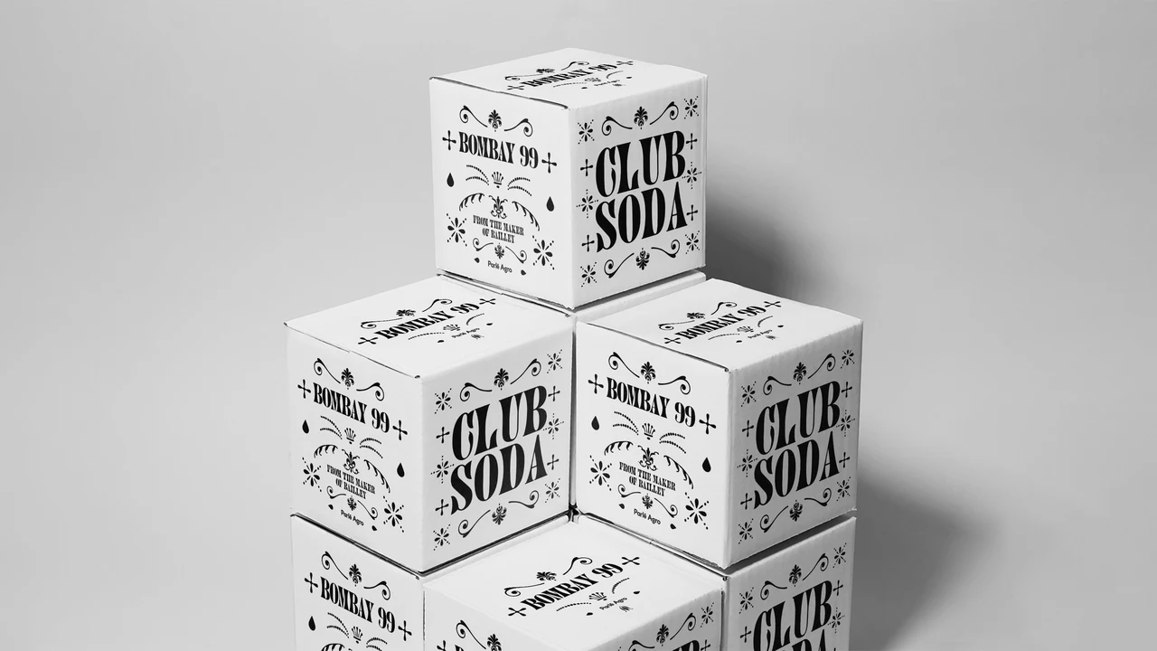 Stacked white Club Soda boxes show condensed black typography on the sides and ornamental symbols on the front.