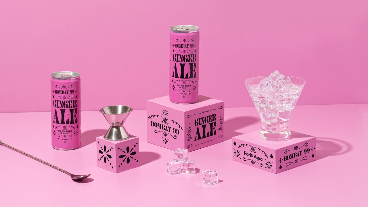 Pink set arranges two Ginger Ale cans, printed boxes, a metal jigger, a long spoon and a glass filled with ice.