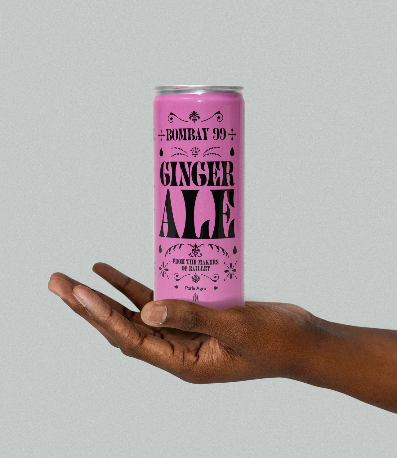 Open hand balances a tall pink Ginger Ale can against a gray background, emphasizing the black ornamental label.