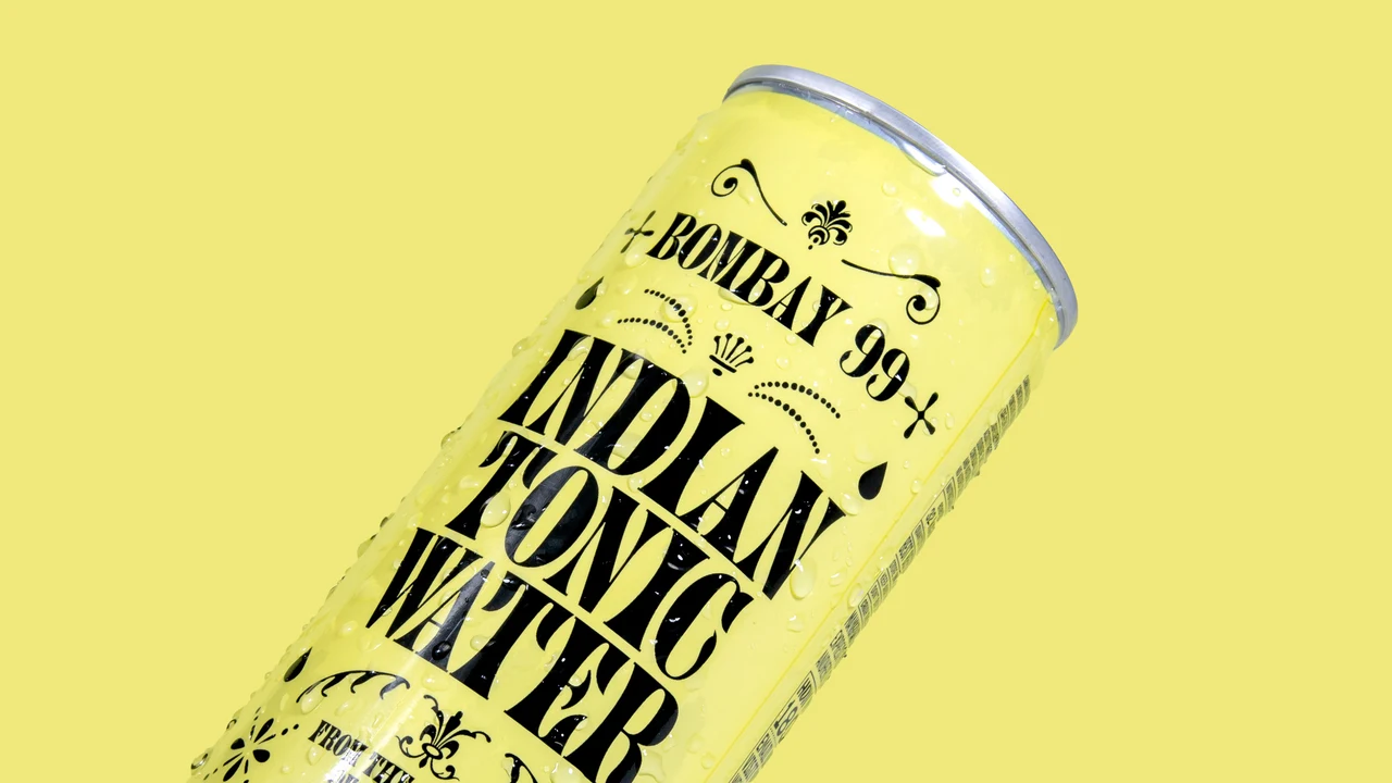 Diagonal close-up of a yellow Indian Tonic Water can highlights tall black lettering, small ornaments and droplets against a yellow background.