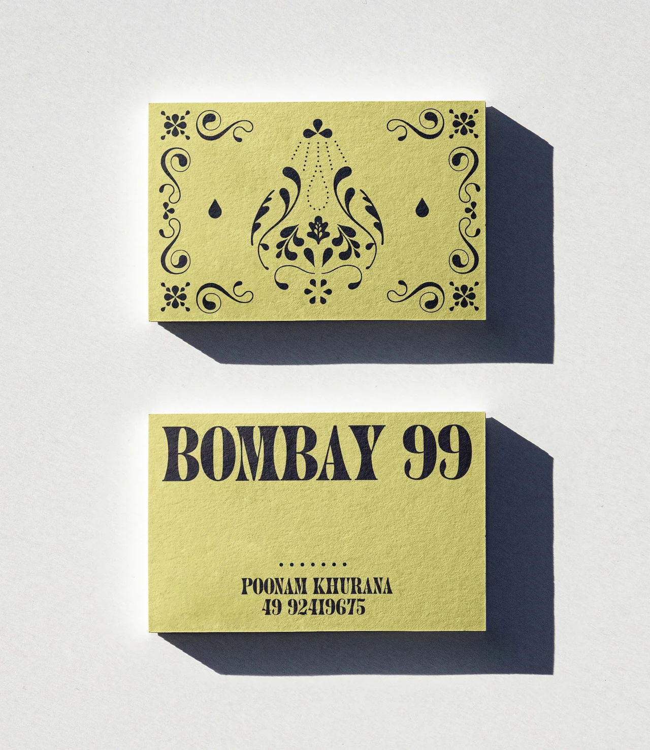 Two yellow cards with deep shadows show an ornamental face and another with Bombay 99 and contact information.