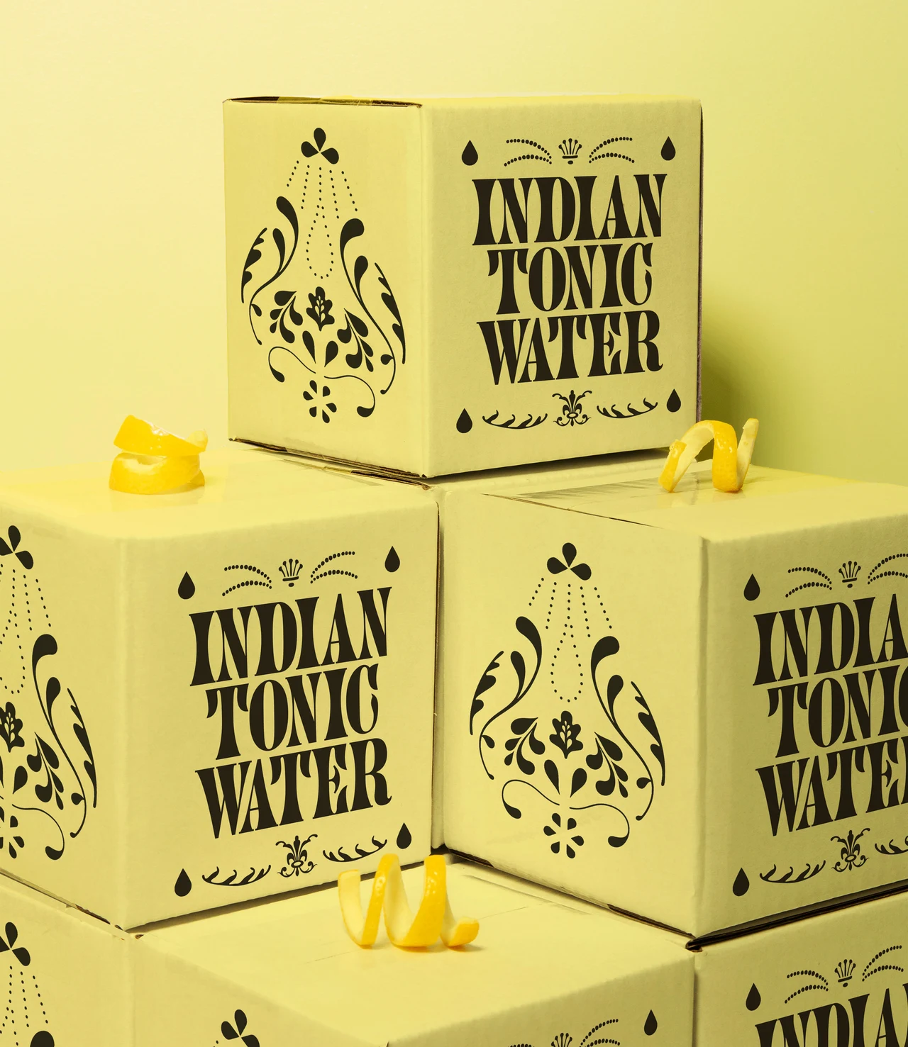 Yellow Indian Tonic Water boxes are stacked with alternating typographic and ornamental faces, among small lemon-peel curls.