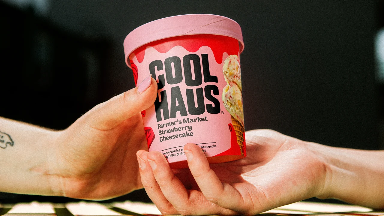 Close-up of hands passing a pink Coolhaus Farmer’s Market Strawberry Cheesecake tub, with its wordmark and flavor label facing the camera.