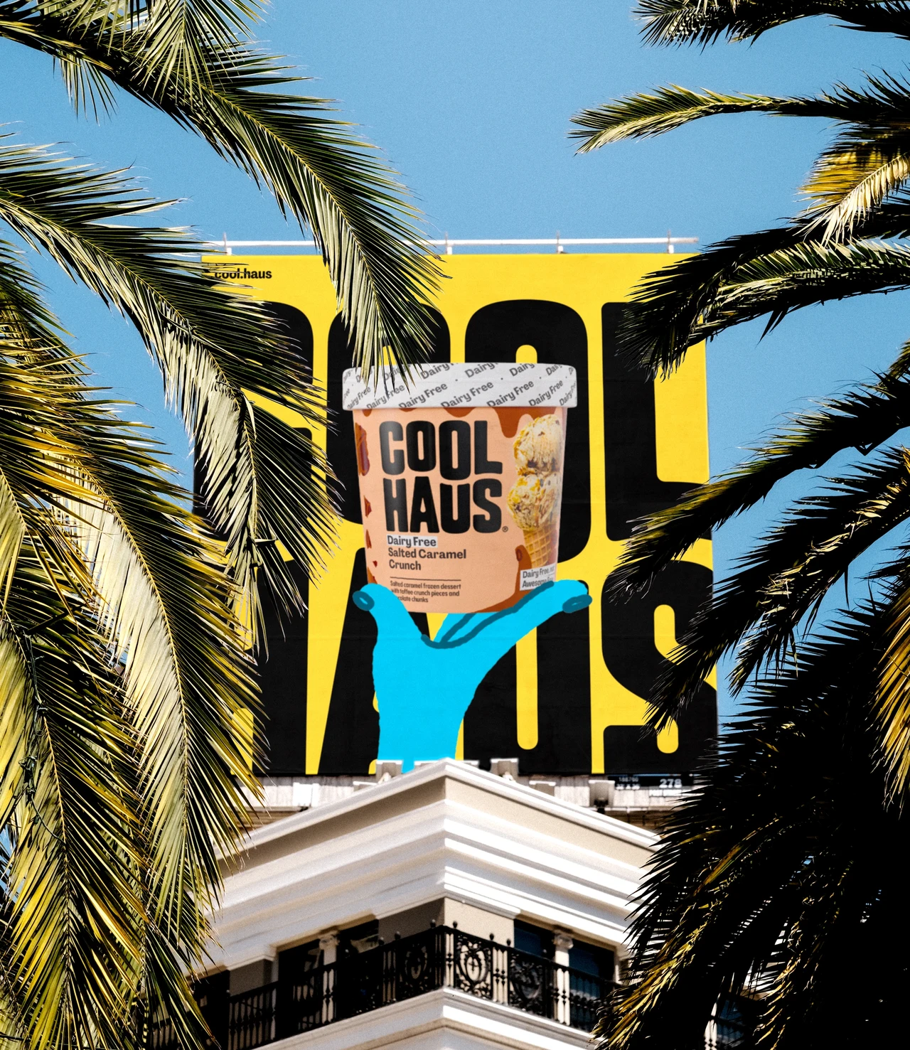 Yellow billboard seen between palm trees shows a Coolhaus tub supported by blue illustrated hands, with giant black lettering behind it.