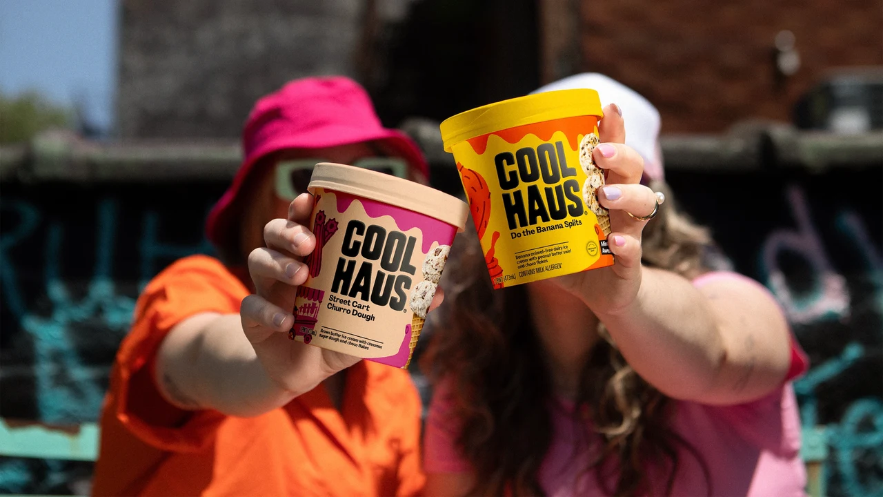 Two people outdoors extend pink and yellow Coolhaus tubs toward the camera; the packaging is sharp while their faces are blurred.
