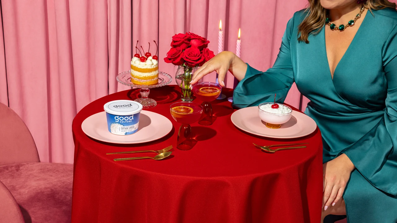 A dinner set with a red round table, pink curtain, roses and candles presents Good Culture tubs beside a person in a teal dress.