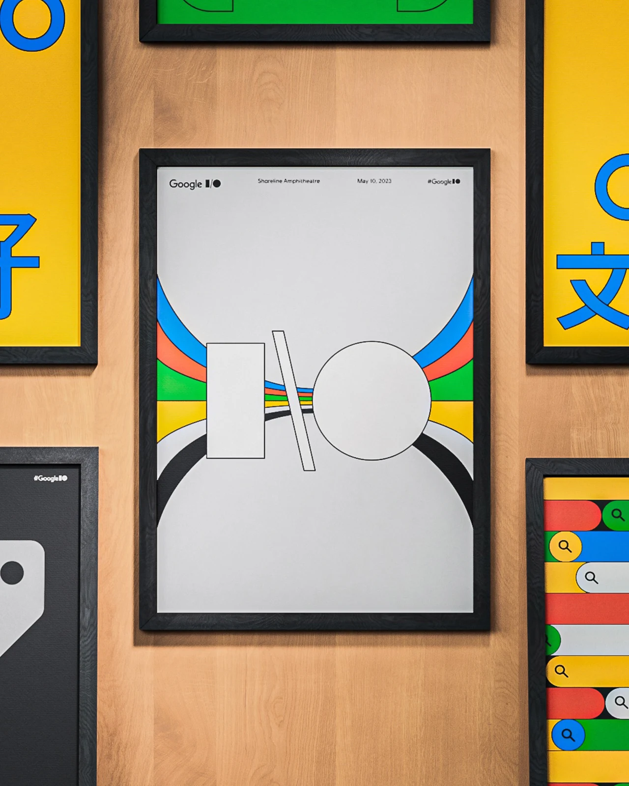 Framed Google I/O poster features an outlined I/O symbol and ribbons in brand colors; it hangs on a wooden wall among other colorful posters.