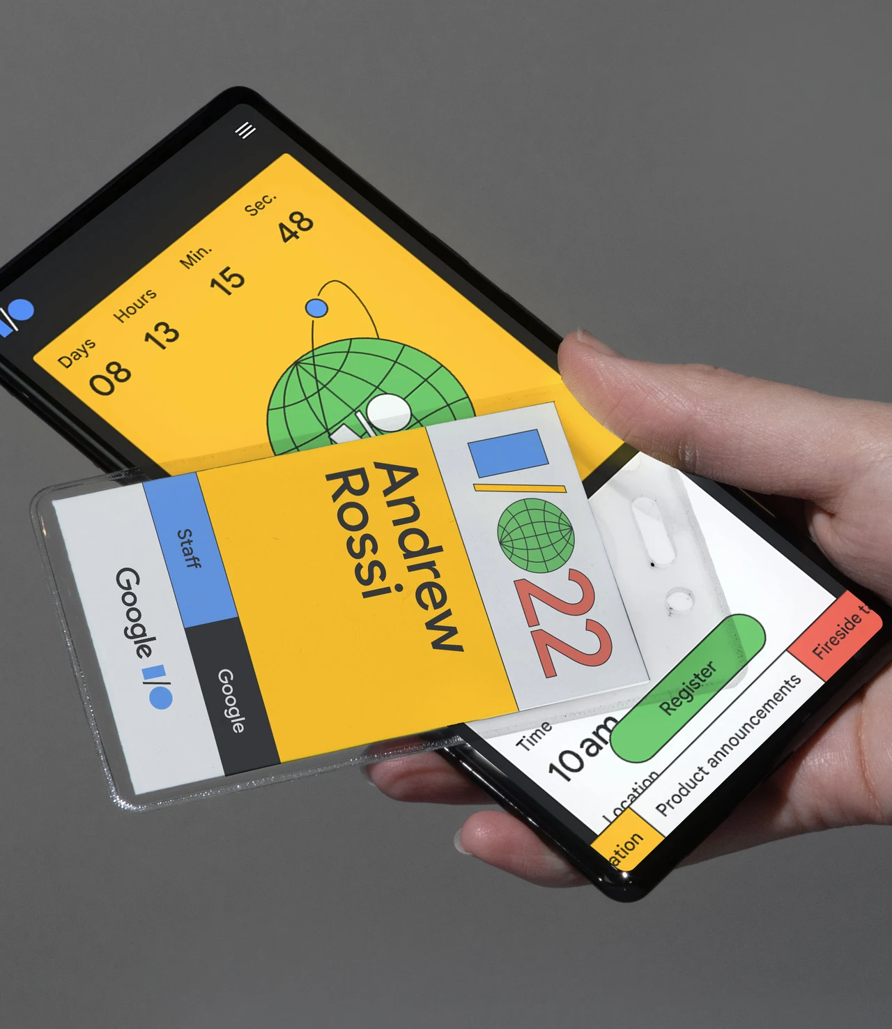 Mão segura dois celulares e um crachá I/O 22; uma tela exibe contagem regressiva em amarelo com globo e a outra mostra informações do evento.