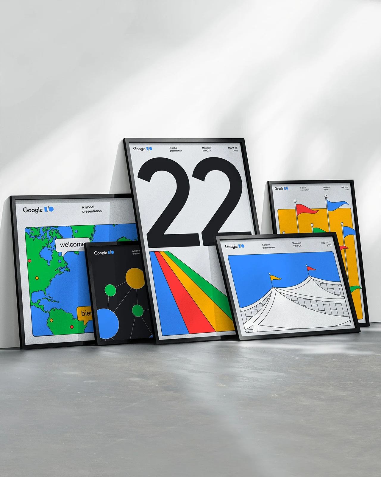 A group of framed Google I/O 2022 posters leaning on the floor combines the number 22, a map, flags, circles and bands in the brand’s four colors.
