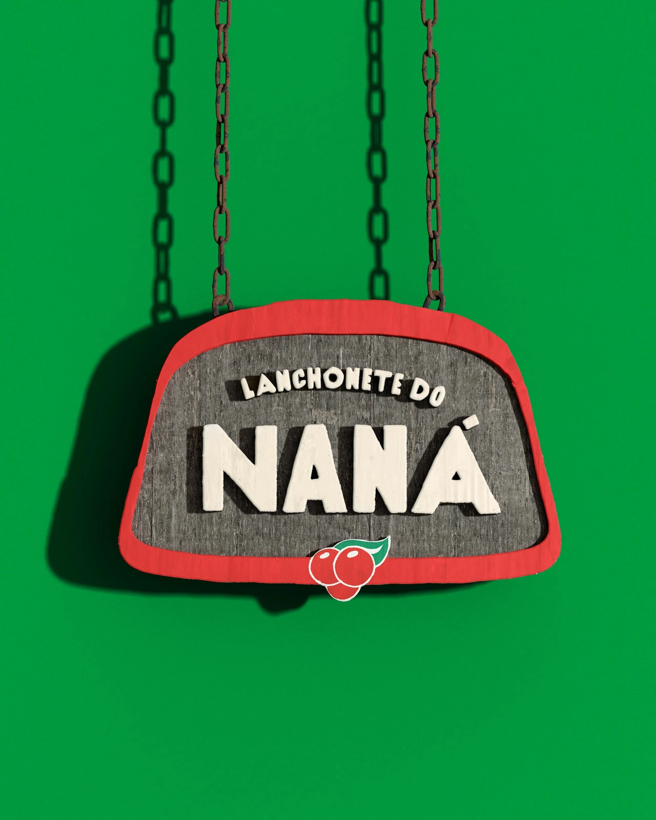 A chain-hung Lanchonete do Naná sign has pale lettering, a red border and a small guaraná symbol against green.