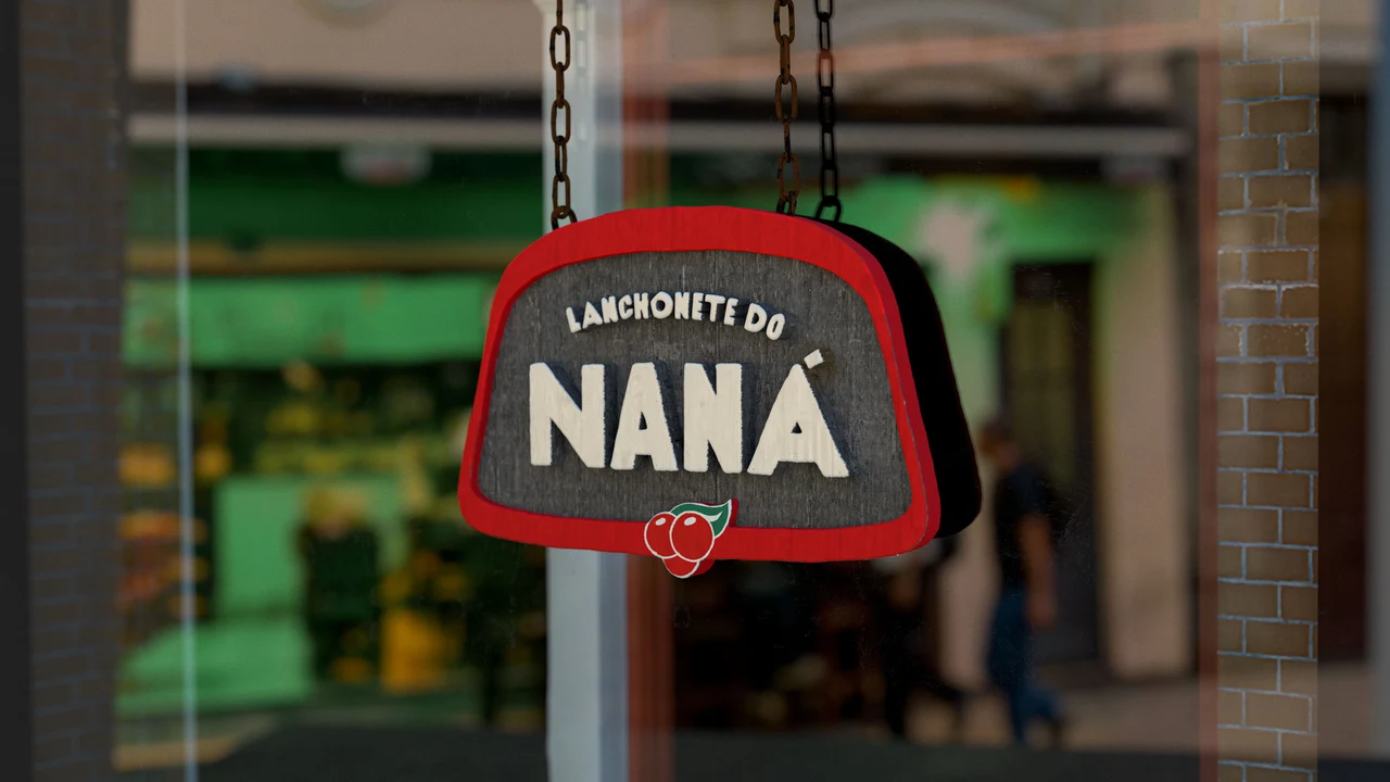 A Lanchonete do Naná sign hangs in front of a blurred counter, showing cream lettering on a dark surface with a red border.