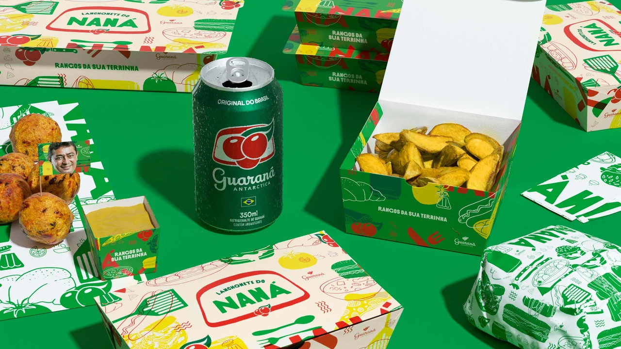 A Guaraná Antarctica can, chips and savory snacks sit among Naná boxes and illustrated wrapping paper on green.