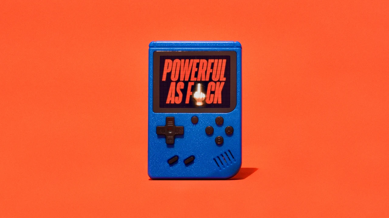 Console portátil azul em estilo retrô aparece sobre fundo laranja e mostra a frase “Powerful as f*ck” em letras condensadas laranja na tela preta.