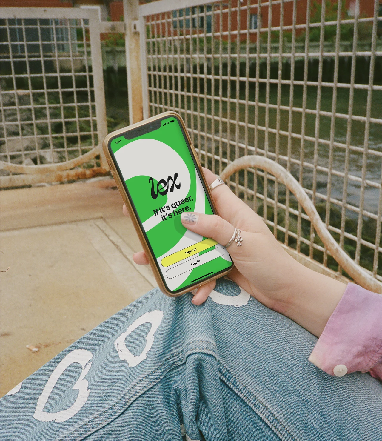 A handheld phone displays the green Lex app entry screen, framed by jeans with white hearts and a metal mesh structure.
