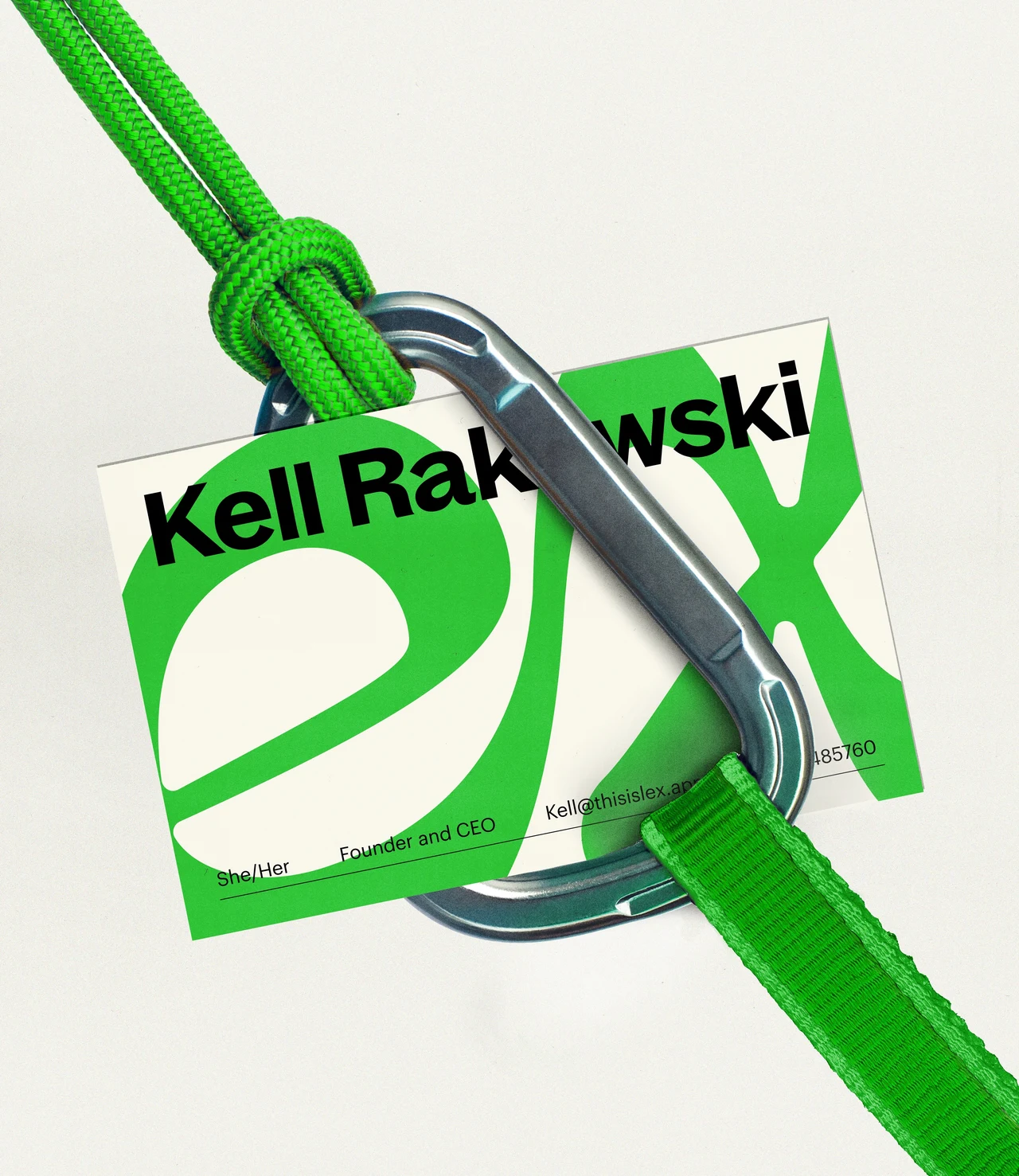 A Kelli Rakowski name badge with a green and cream Lex pattern is attached to a large metal carabiner and green cord.
