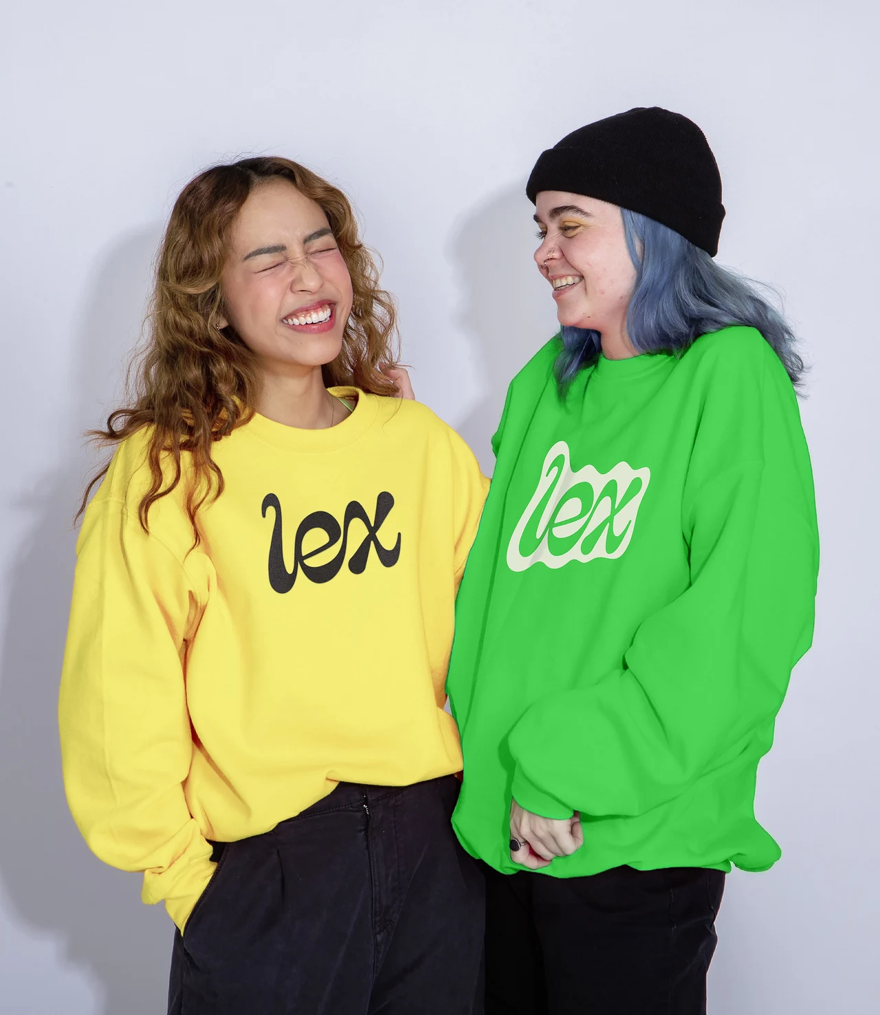 Two people smile at one another while wearing yellow and green sweatshirts with the Lex wordmark printed on their chests.