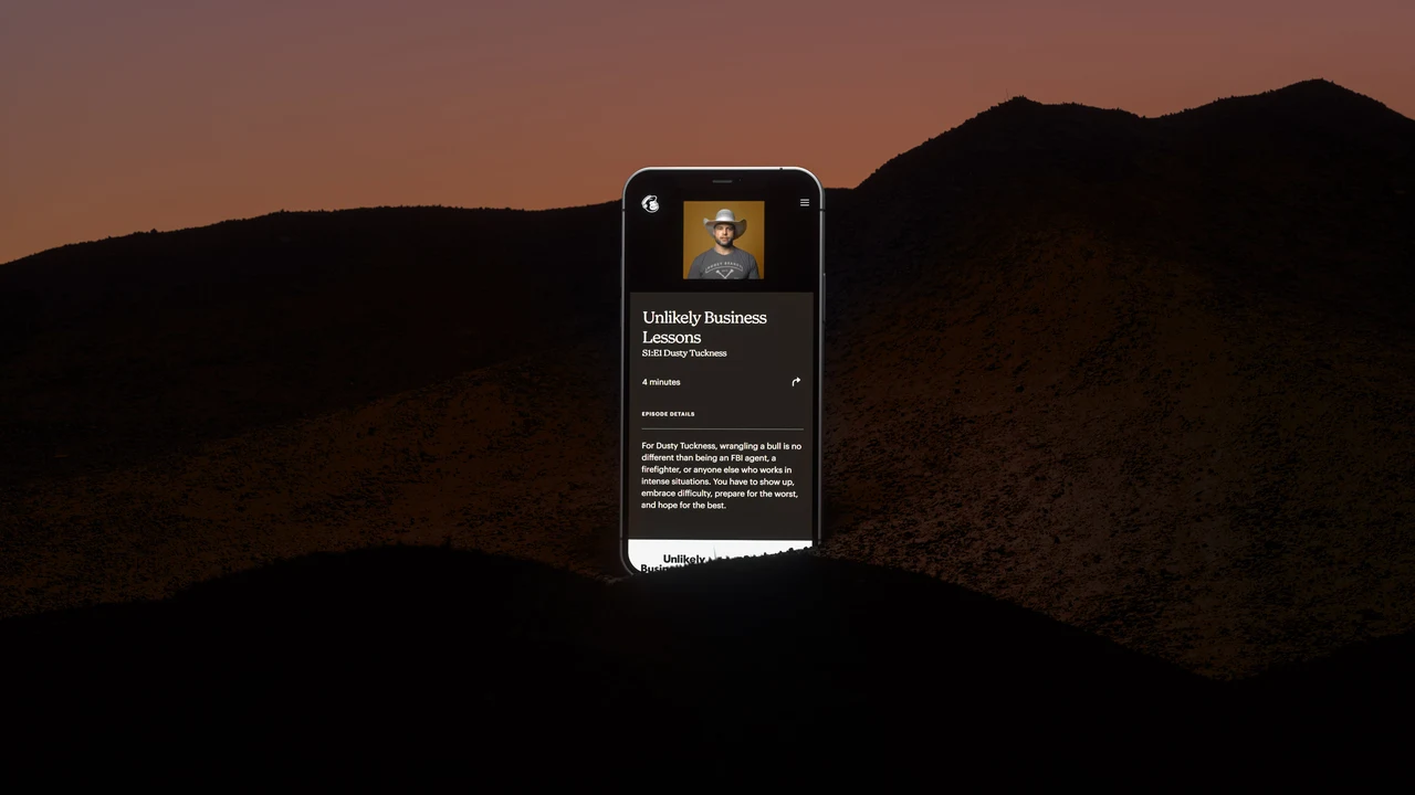 A phone displaying a Mailchimp program page stands in a dark mountain landscape beneath an orange sky.