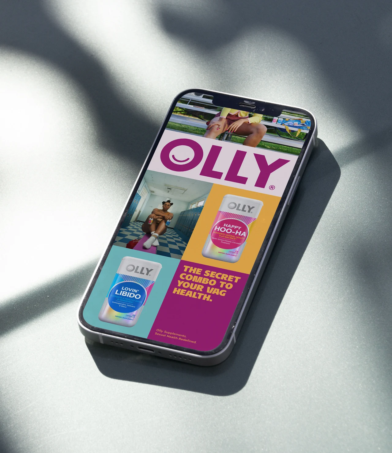 Phone on a shadowed surface displays an OLLY campaign collage with a magenta wordmark, photographs and bottles arranged in colored blocks.