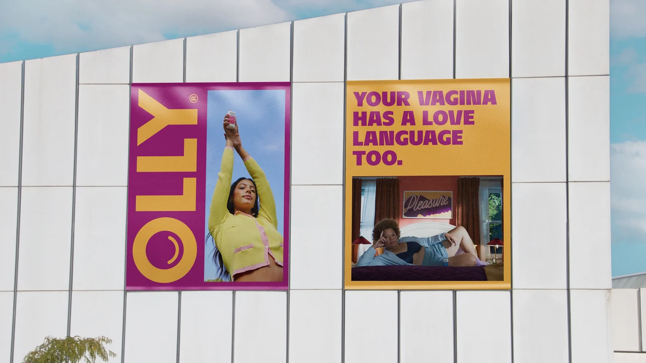 Two posters on a white facade pair a vertical OLLY name and a woman’s photograph with yellow love-language messaging above a bedroom scene.