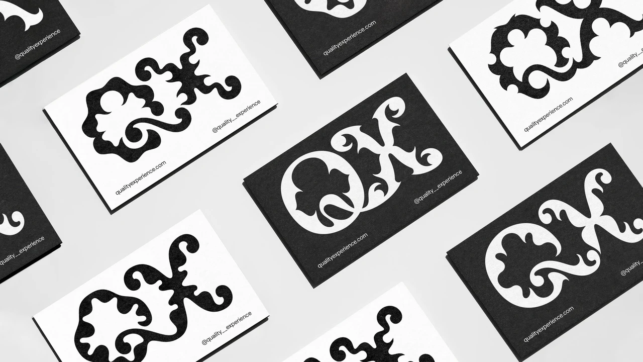 Black and white business cards present ornamental variations of the QX monogram, arranged diagonally on a pale surface.
