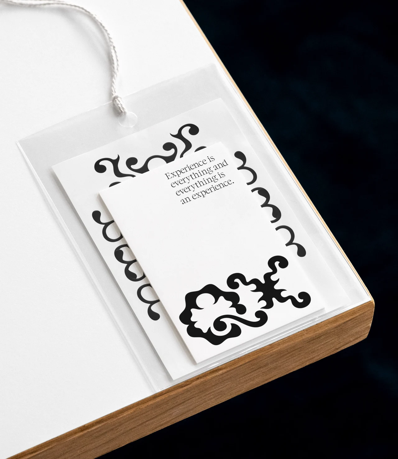 White card with a QX logo, text and black ornaments presented inside a transparent badge holder with a white cord on a table.