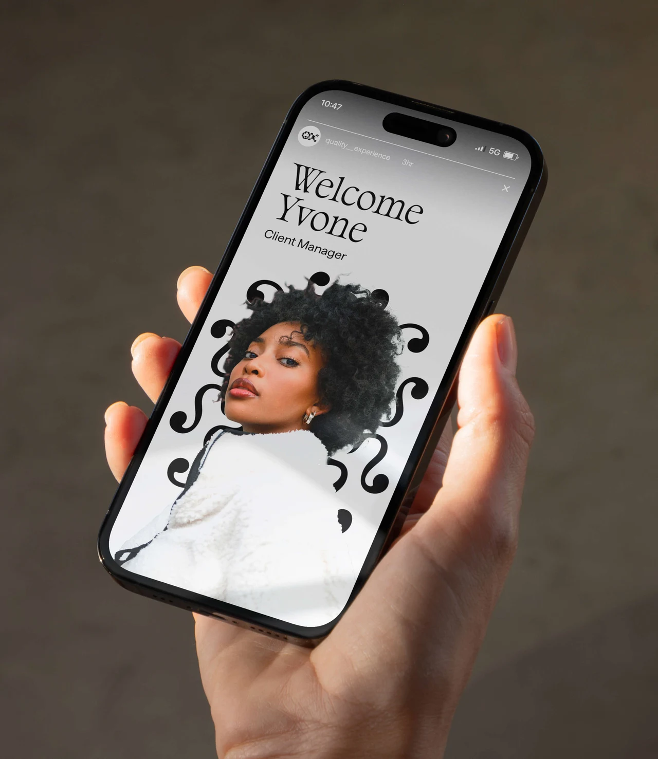 A hand holds a smartphone with a quality_experience Story: “Welcome Yvone”, the Client Manager role and a woman's portrait surrounded by black ornaments.
