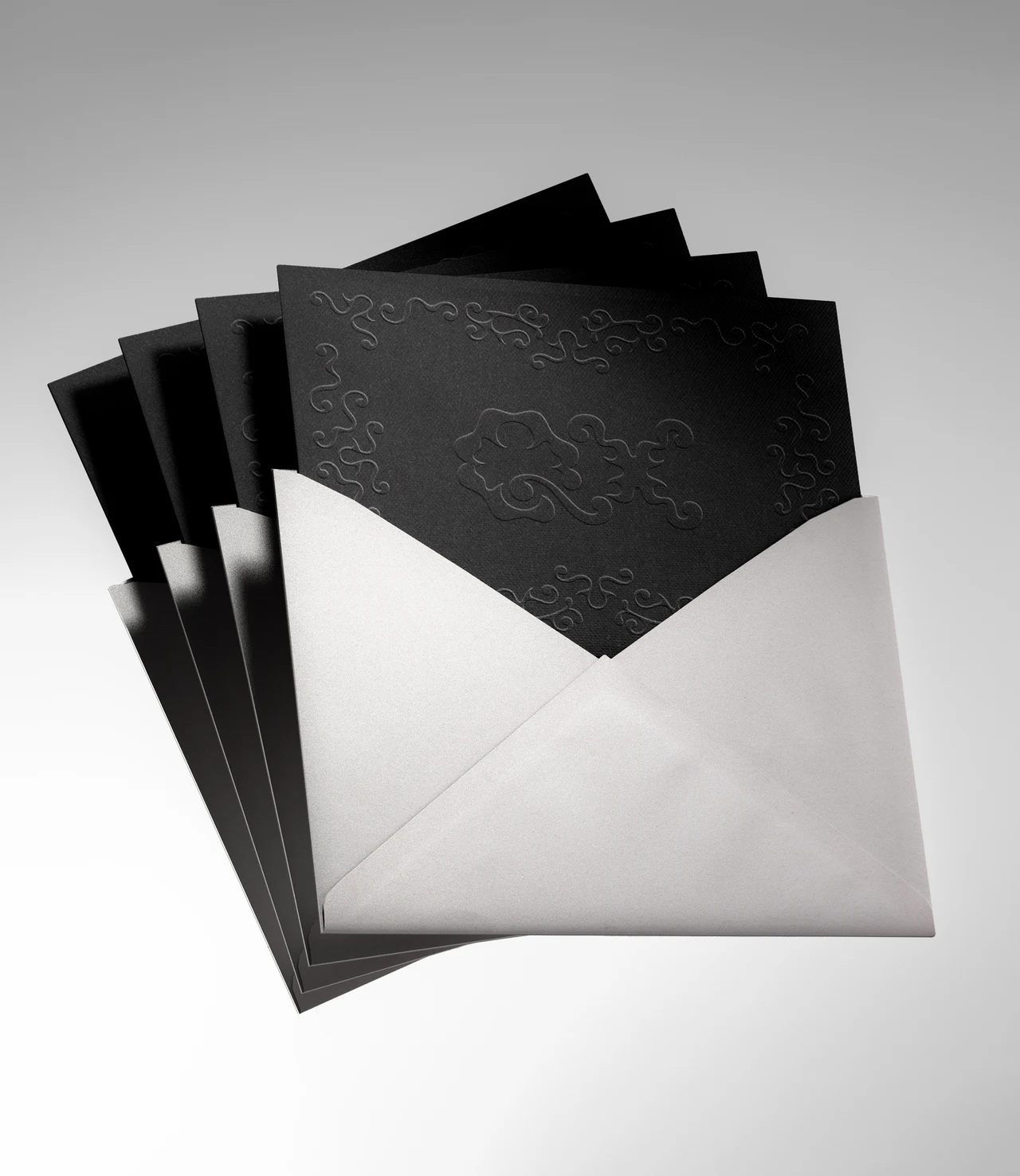 Pale envelopes contain black cards with subtle embossed QX patterns, arranged in a fan on a light gray background.