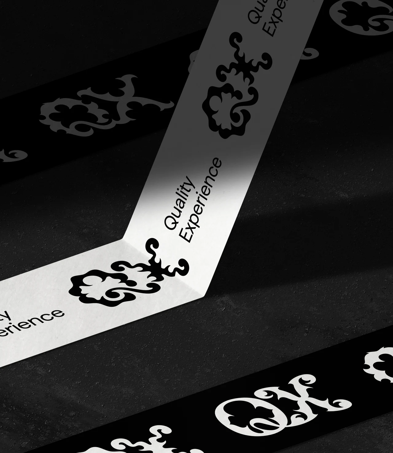 Wide black and white strips with QX monograms and “Quality Experience” cross a dark surface in diagonals and folds.