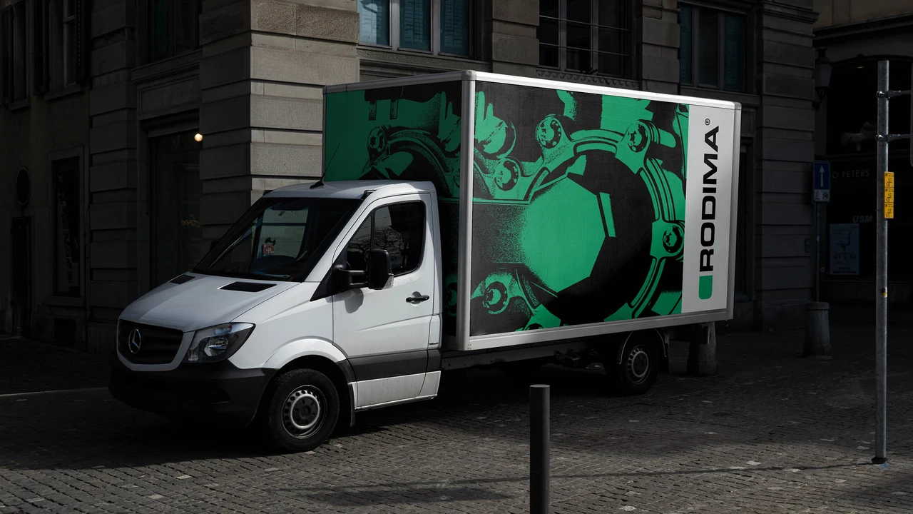A white truck on an urban street carries a green and black wrap with an enlarged mechanical component and Rodima branding.