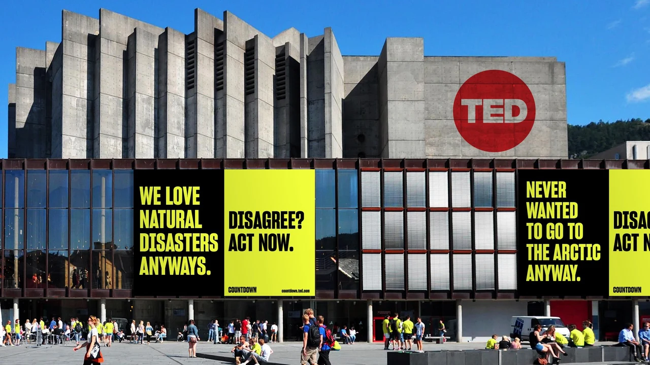 Event-center facade with a red TED symbol carries black and lime-yellow banners with provocative messages about natural disasters and climate action.