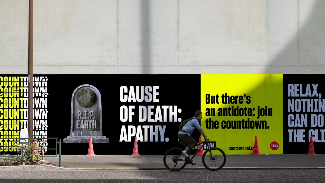 Urban hoarding combines repeated Countdown lettering, an R.I.P. Earth gravestone and messages about apathy and climate action, with a cyclist passing in front.