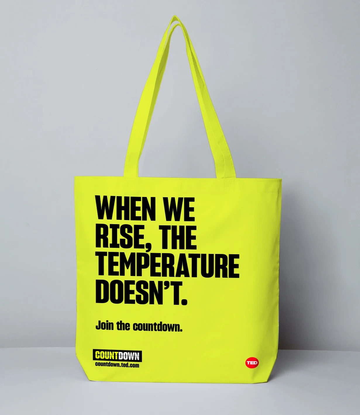 Lime-yellow tote bag displays When we rise, the temperature doesn’t in black typography, with a Countdown signature and TED badge.