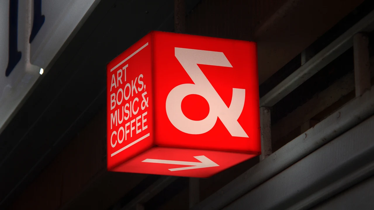 Glowing red cube sign on a facade displays a large white ampersand and “Art Books Music & Coffee”.