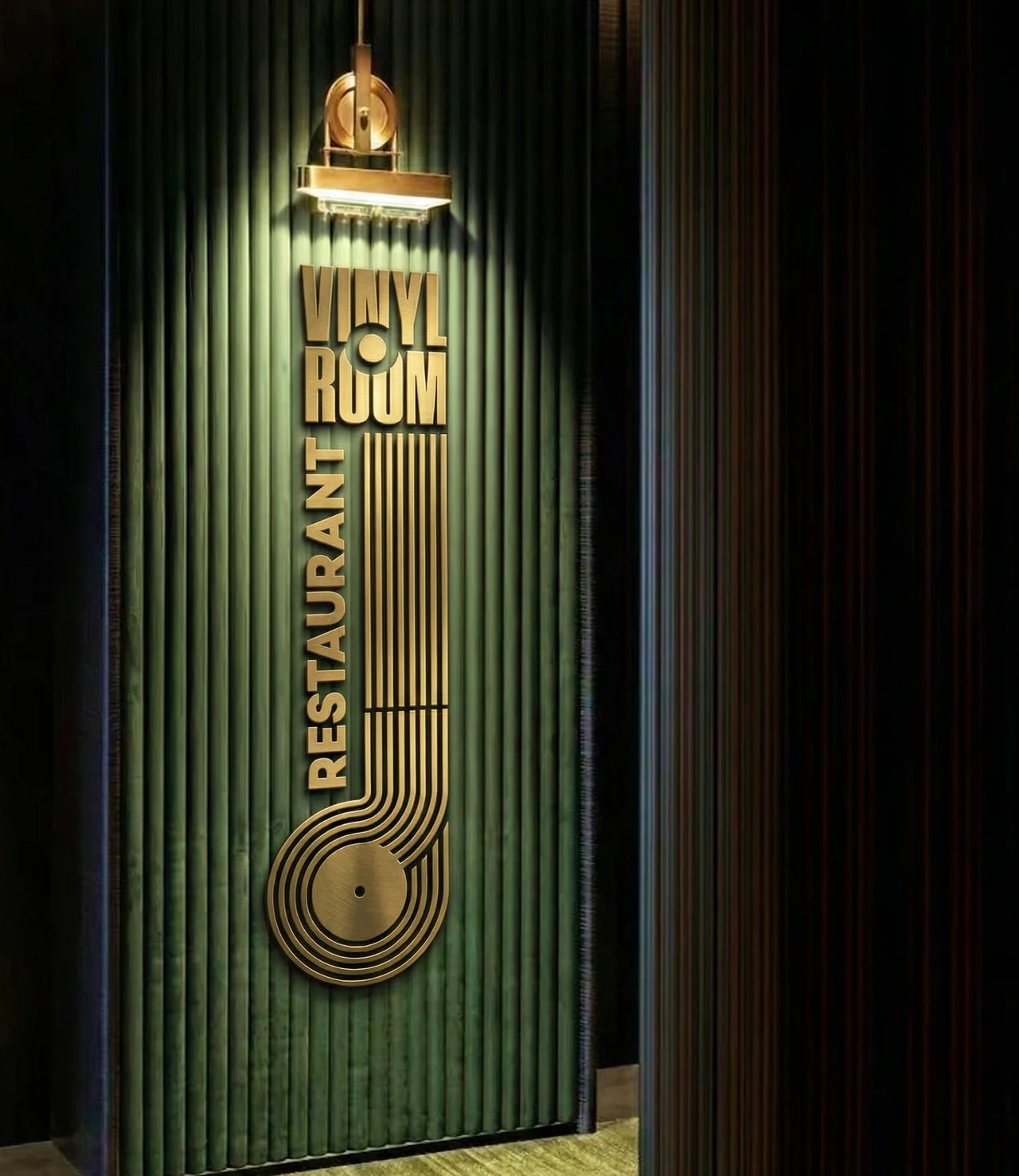 Brass Vinyl Room Restaurant sign on a green fluted wall: the wordmark above vertical Restaurant lettering and a line pattern curving into a record, lit by a brass picture light.